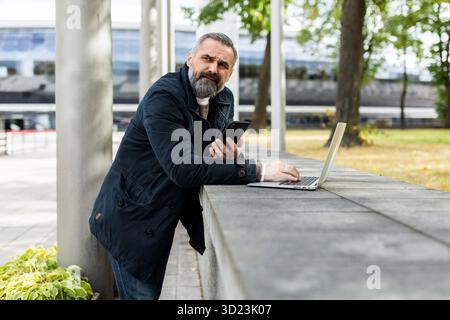 Fünfzig Jahre alter Geschäftsmann, der im Park an Laptops arbeitet Stockfoto