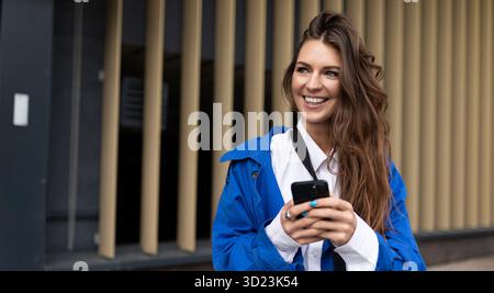Porträt einer charmanten Frau mit einem Handy in den Händen auf dem Hintergrund der Fassade des Business Centers Stockfoto