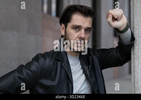 Ein ernster Mann mit negativen Emotionen steht auf seinem Ellenbogen und blickt in die Ferne draußen Stockfoto