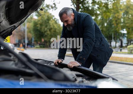 Reifer Mann, der versucht, eine Panne zu finden, die sich über den Motor in der Stadt beugt Stockfoto