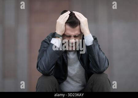 Ein Mann mit Migräneanfall sitzt und schreit Stockfoto