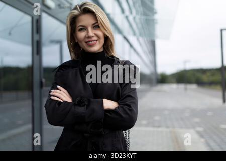 Porträt einer erfolgreichen Geschäftsfrau in einem schwarzen Business-Anzug neben dem Eingang zum Bürogebäude Stockfoto