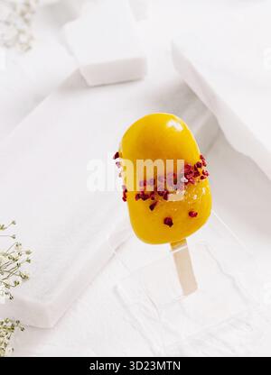 Köstliche gefrorene Mango-Leckereien, dekoriert mit essbaren Blumen auf einer weißen Oberfläche Stockfoto