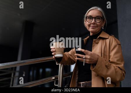 Reife weiße Geschäftsfrau mit einer Tasse Kaffee draußen Stockfoto