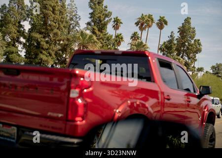 Roter Pickup-Truck parkte neben hohen Palmen unter klarem blauem Himmel. Kalifornien, USA Stockfoto