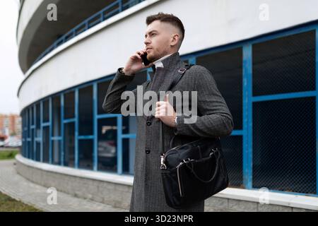 Ein junger, stilvoller Geschäftsmann spricht gut am Telefon vor dem Hintergrund des Parkplatzes Stockfoto