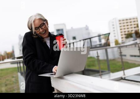 Geschäftsfrau, die im Freien mit einem Laptop und einer Tasse Kaffee arbeitet Stockfoto