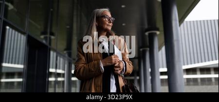 Eine ältere Geschäftsfrau im mittleren Alter mit Brille geht mit einem Laptop zur Arbeit Stockfoto