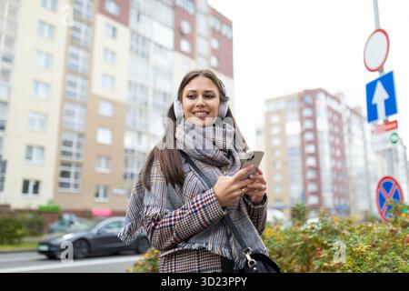 Porträt einer jungen Frau in Kopfhörern mit Handy vor dem Hintergrund der Stadt Stockfoto