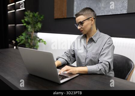 Erfolgreiche Programmiererin, die in einem eleganten Büro hinter einem Laptop arbeitet und eine neue Anwendung entwickelt Stockfoto
