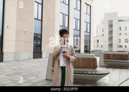 Junge afroamerikanische Geschäftsfrau, die auf einem Handy vor dem Hintergrund eines Bürozentrums spricht Stockfoto