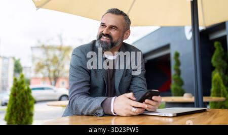 Porträt eines starken grauhaarigen Geschäftsmannes neben dem Büro mit einem Telefon in der Hand Stockfoto