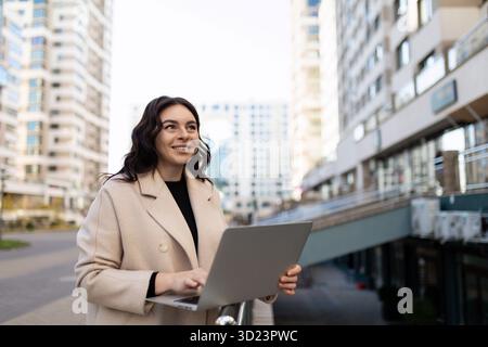 Erfolgreiche selbstbewusste moderne Unternehmerin mit einem Laptop in der Hand arbeitet online im IT-Büro mit einem Lächeln auf ihrem fac Stockfoto