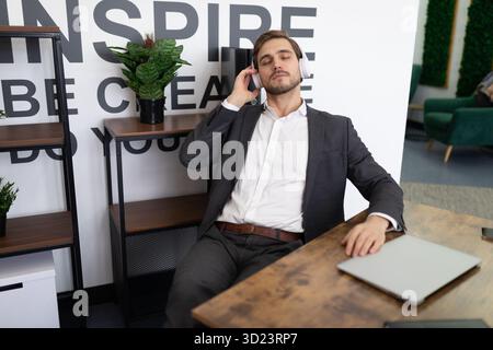 Ein Geschäftsmann spricht auf einem Handy und sitzt imposant auf einem Stuhl Stockfoto