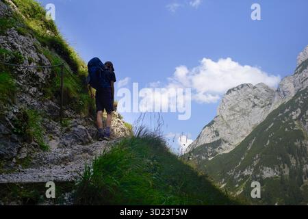 Wanderer mit Rucksack auf einem Bergpfad unter einem hellblauen Himmel mit majestätischen Gipfeln. Salzkammergut, Dachsteingebirge, Österreich Stockfoto