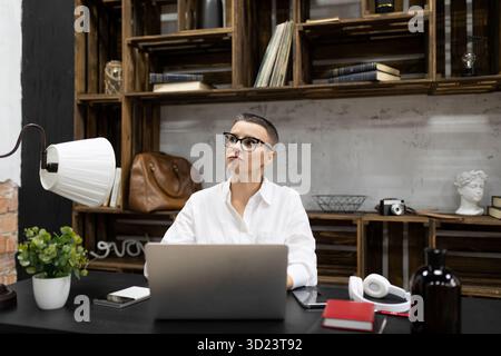 Erwachsene weiße Frau mit kurzen Haarschnitten in Brille arbeitet an einem Laptop im Büro Stockfoto