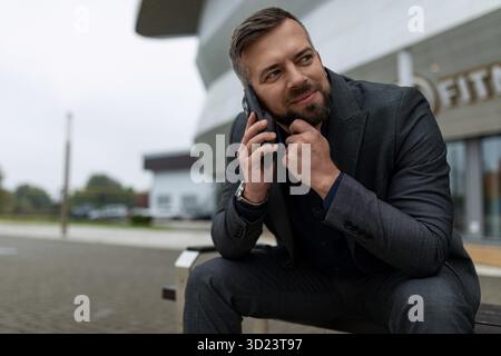 Ein erwachsener Geschäftsmann, der draußen mit einem nachdenklichen Ausdruck telefoniert Stockfoto