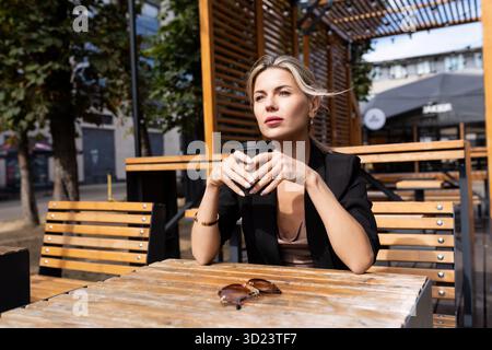 Stilvolle nachdenkliche Frau mittleren Alters, die Kaffee in einem Café auf der Straße trinkt Stockfoto