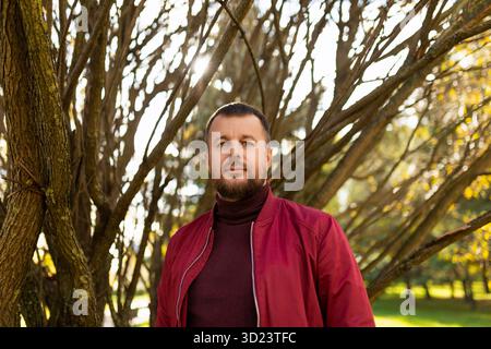 Porträt eines starken bärtigen Mannes in einer roten Jacke im Herbstpark Stockfoto