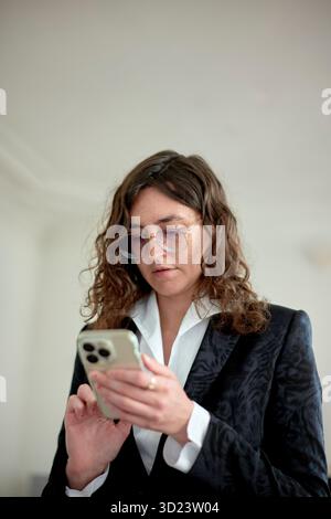 Frau in Geschäftskleidung, die ein Smartphone mit Fokus auf dem Bildschirm verwendet. Brüssel, Belgien Stockfoto