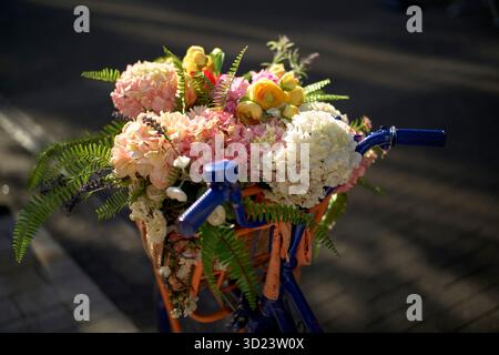 Fahrradkorb gefüllt mit bunten Blumen und Grün unter sanftem Sonnenlicht. Brüssel, Belgien Stockfoto