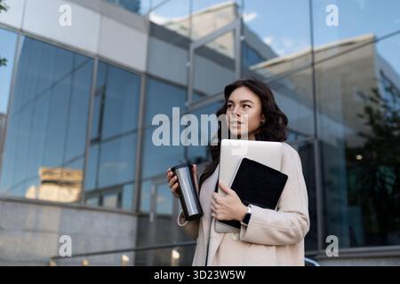 Geschäftsfrau mit einem Laptop und einem Glas Kaffee vor dem Hintergrund der Glasfassade des Büros Stockfoto