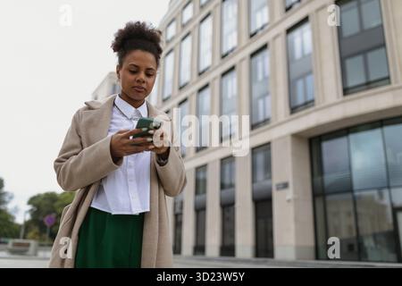 Die verwirrte 30-jährige afroamerikanische Geschäftsfrau schaut in ein Mobiltelefon im Hintergrund des Bürozentrums Stockfoto