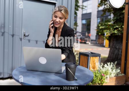 Junge erfolgreiche Frau, die auf der Straße an einem Laptop arbeitet Stockfoto