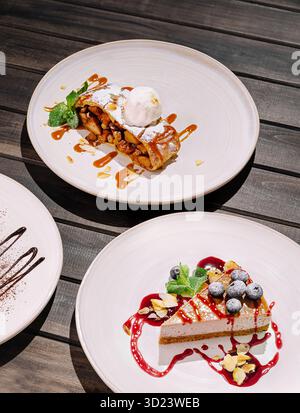 Ein verführerisches Dessert-Arrangement zeigt eine Scheibe Käsekuchen mit Beeren und einen mit Früchten gefüllten Teig mit Sauce, serviert auf Simple Stockfoto