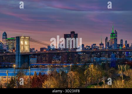 Brooklyn Bridge und New York City Skyline bei Sonnenuntergang mit leuchtenden Himmel- und Stadtlichtern. New York City, NY, USA Stockfoto