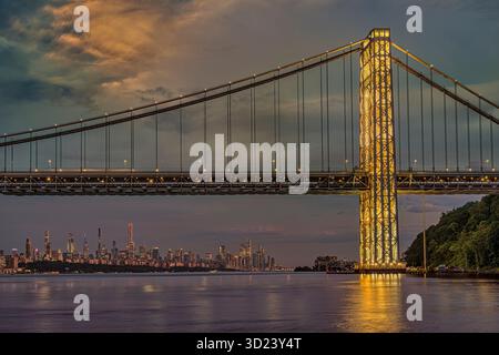 Beleuchtete Brücke bei Sonnenuntergang über einem ruhigen Fluss mit einer Skyline der Stadt in der Ferne. New York City, NY, USA George Washington Bridge, Hudson River Stockfoto