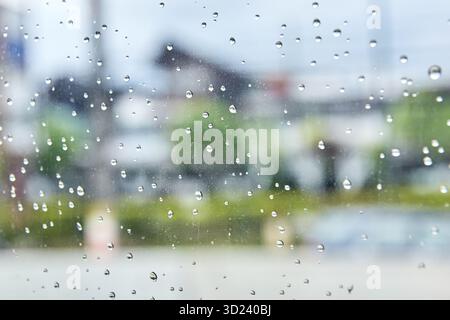Regentropfen am Fenster mit verschwommenem urbanem Hintergrund, die einen regnerischen Tag festhalten Stockfoto