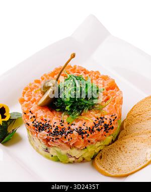 Frischer Lachstartar mit Avocado und Algen, serviert auf einem weißen Teller Stockfoto