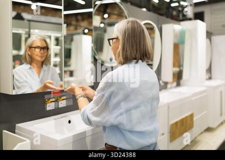 Frau untersucht die Badezimmerausstattung in einem modernen Wohnhaus während des Einkaufs tagsüber Stockfoto