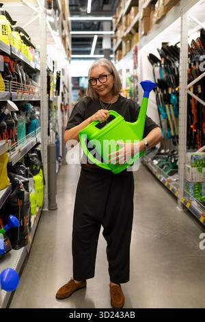 Frau hält große grüne Gießkanne in der Hauswerkstatt mit Gartenwerkzeugen und -Zubehör Stockfoto