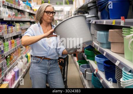 Frau, die in einem Ladengang nach Lagerbehältern sucht, während sie einen grauen Eimer auswählt Stockfoto