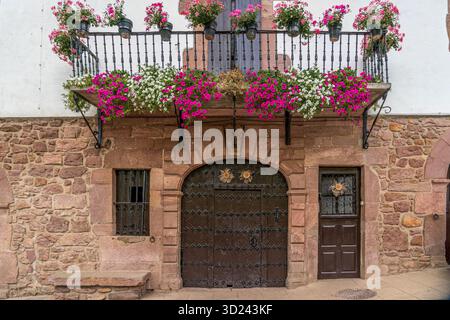 Traditionelle spanische Steinfassade mit bunten Blumen-Balkon, rosa und weiße Geranien, rustikale Holztür, Architektur Stockfoto