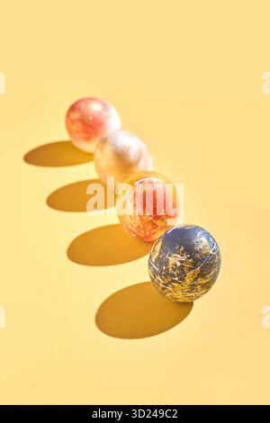 Bunte Marmorkugeln in warmen Tönen auf gelbem Hintergrund werfen Schatten Stockfoto