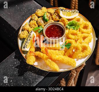Eine appetitliche Auswahl an frittierten Meeresfrüchten auf einem Teller, mit Garnelen, Calamari und Austern, garniert mit Zitrone und Kräutern. Perfekt für s Stockfoto