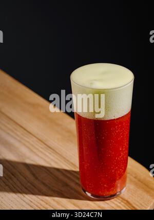 Erfrischendes rotes Getränk in einem Glas mit schäumendem Kopf auf Holztisch Stockfoto
