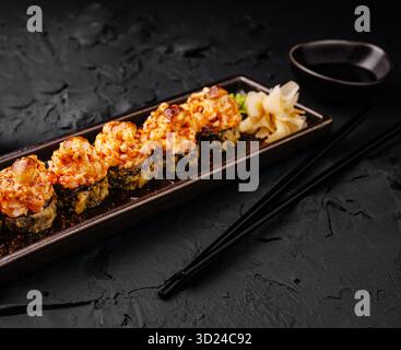 Sushi-Brötchen mit Garnelenbelag, serviert auf einem dunklen Teller im Restaurant Stockfoto