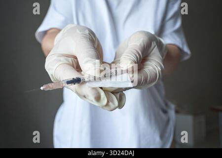 Weibliche Krankenschwester, die Spritze in Schutzhandschuhen für die medizinische Injektion hält Stockfoto