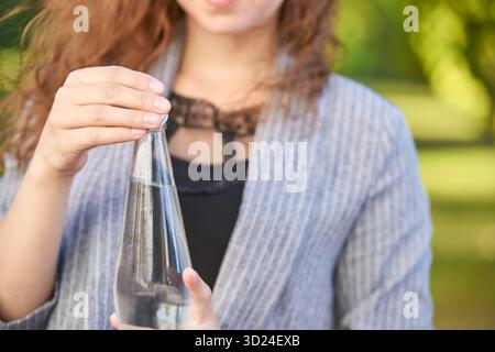 Junge hispanische Frau, die Glaswasserflasche draußen in einer Hand hält Stockfoto