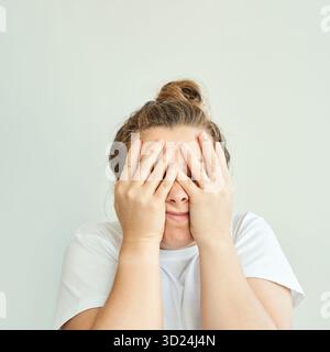 Weibliche kaukasische Erwachsene mit Händen, die das Gesicht in Frustration in lässiger Kleidung bedecken Stockfoto