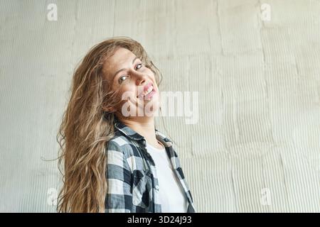 Lächelnde kaukasische junge Erwachsene Frau mit langen Haaren in kariertem Hemd Stockfoto