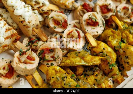 Verschiedene gegrillte Hähnchenspieße mit Soße und Kräutern, auf einem Teller zum Servieren angeordnet. Stockfoto