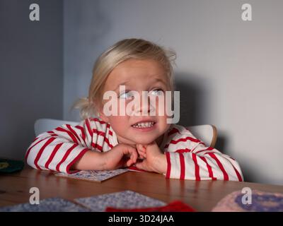 Das vierjährige Mädchen sitzt am Tisch und wartet auf das Mittagessen. Sie hat Hunger Stockfoto