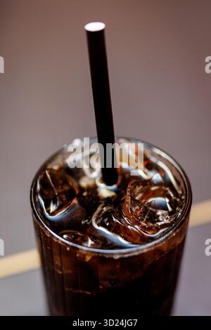 Macro shot of a cold glass of cola filled with ice cubes and a straw, showing reflections and bubbles on the surface. Stockfoto