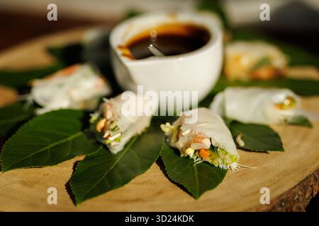 Frische vietnamesische Frühlingsrollen mit Garnelen, Gemüse und Nudeln auf grünen Blättern mit Sojasauce in einer weißen Schüssel. Stockfoto