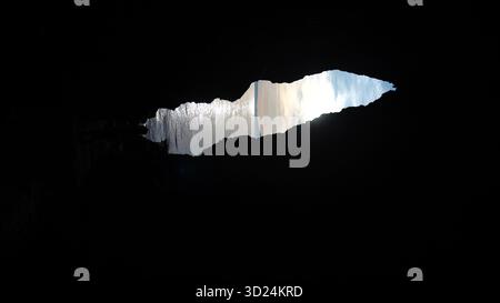 Eine dunkle Höhle mit einem Loch in der Decke. Das Loch wird von der Sonne beleuchtet. Die Höhle ist leer und der Himmel ist klar Stockfoto